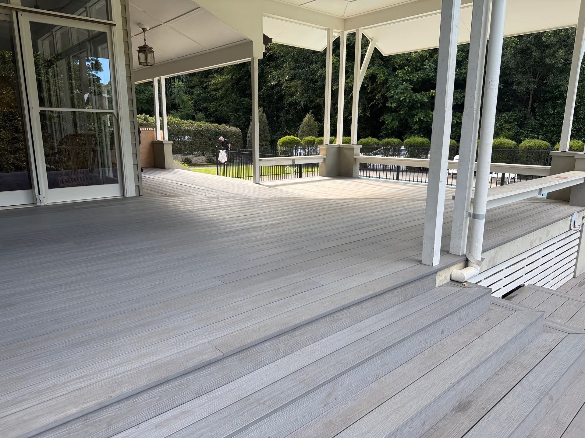 Spacious covered deck with gray composite decking, white columns, and views of landscaped grounds and trees beyond the railing.