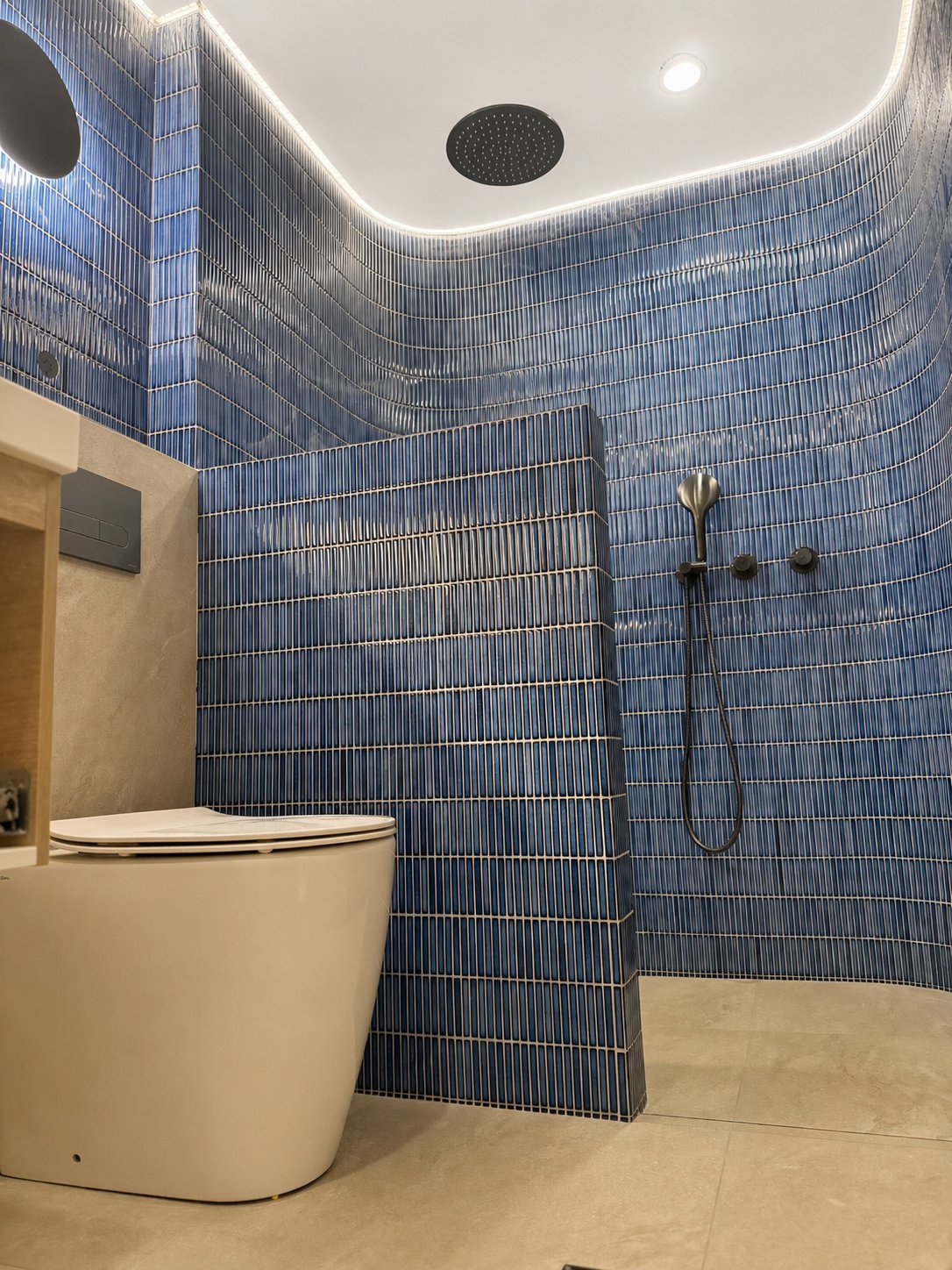Modern bathroom with blue tile walls, white toilet, walk-in shower with rainfall showerhead, and recessed ceiling lighting.